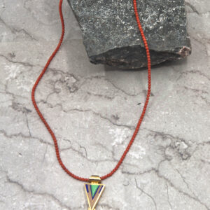 A necklace with a triangle shaped pendant on a red cord.