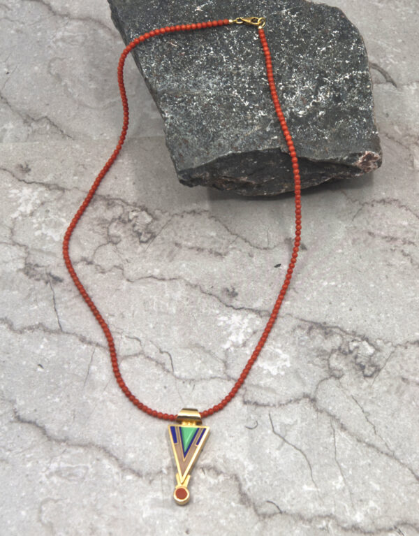 A necklace with a triangle shaped pendant on a red cord.