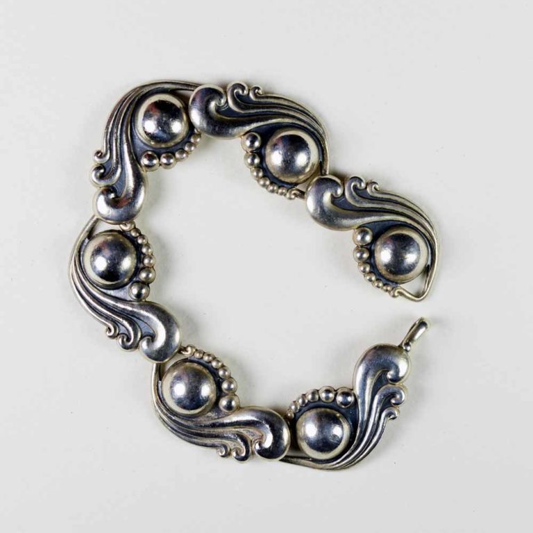 A silver bracelet with swirling designs and balls.