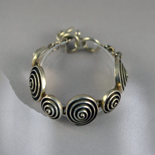 A silver bracelet with five circles on it.