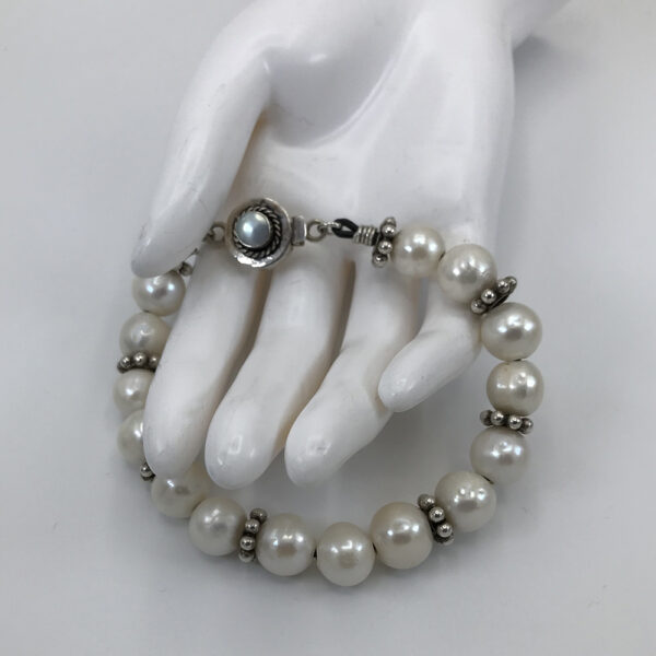 A white hand holding a pearl bracelet with a black stone.