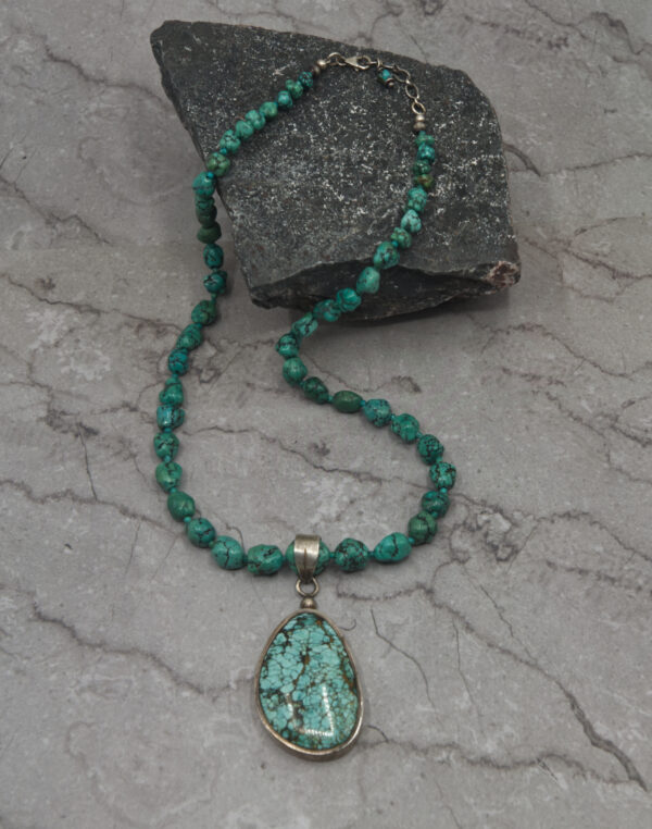 A necklace with a turquoise stone and silver pendant.