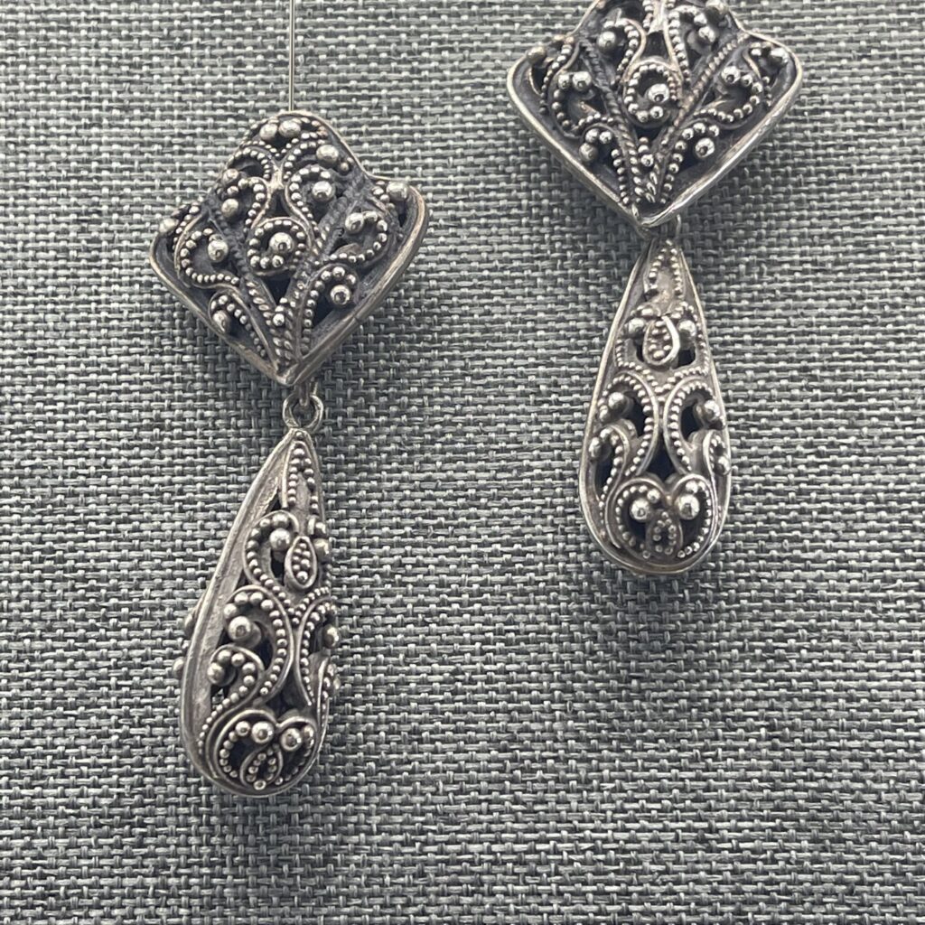 A pair of silver earrings on top of a gray cloth.