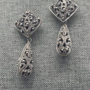 A pair of silver earrings on top of a gray cloth.