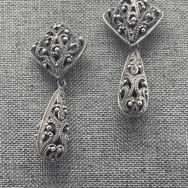 A pair of silver earrings on top of a gray cloth.