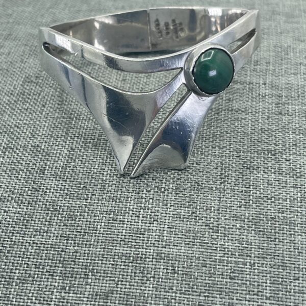 A silver bracelet with a green stone on it.