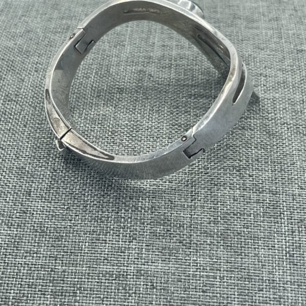 A silver bracelet sitting on top of a gray cloth.