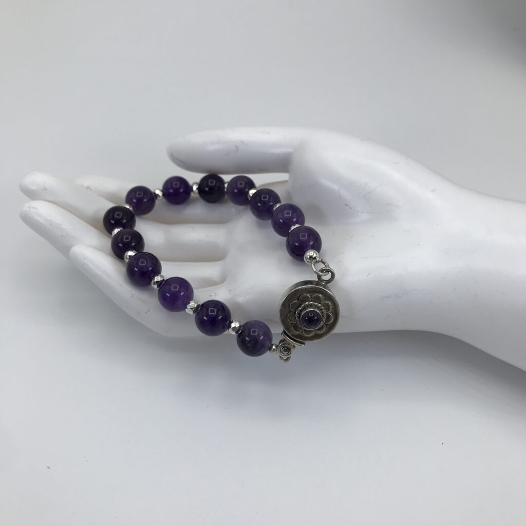 A hand is holding a bracelet with purple beads.