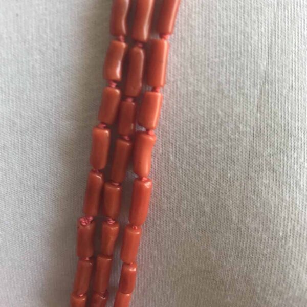 A long necklace of red coral beads on a white wall.