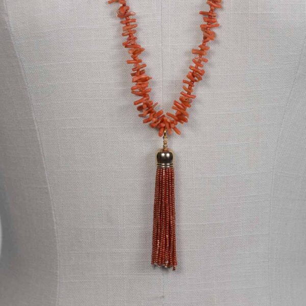 A long necklace with an orange bead and a gold tassel.