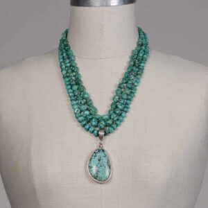 A necklace with three strands of turquoise beads and a large pendant.