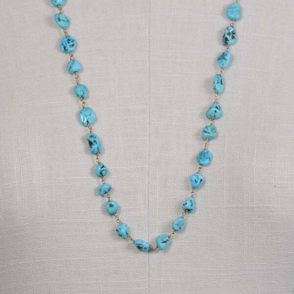 A long necklace of turquoise beads on a white cloth.