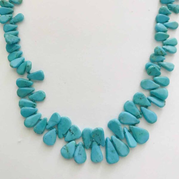 A necklace of turquoise beads is shown on a white surface.