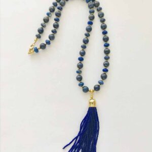 A blue tassel necklace sitting on top of a white table.