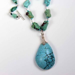 A turquoise necklace with a large pendant on it.