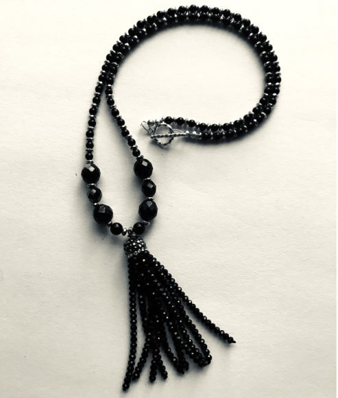 A black beaded necklace with a silver tassel.