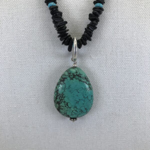 A turquoise stone is on top of black beads.