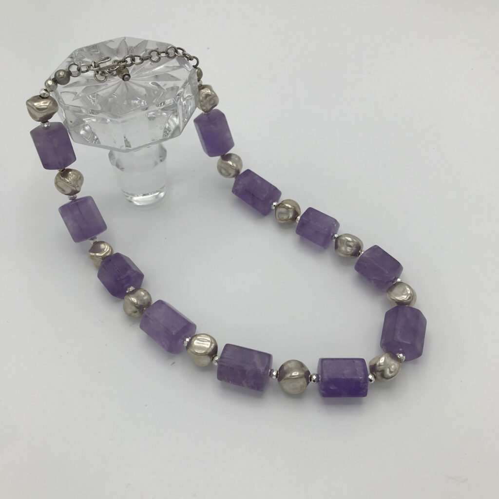 A necklace of purple and silver beads on a white table.