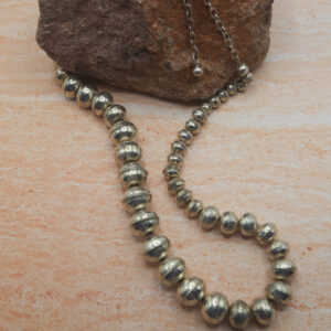 A long necklace of silver beads is sitting on the ground.