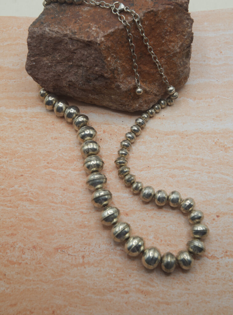 A long necklace of silver beads is sitting on the ground.